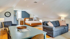 Une chambre de style loft moderne, avec un lit en mezzanine, un coin repas comprenant une table et des chaises, et un canapé gris.