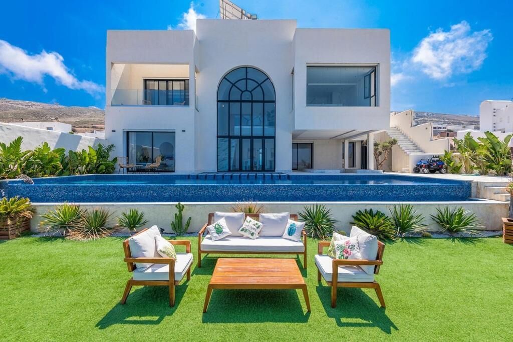 A modern two-story house with a swimming pool, outdoor seating, and a view of the landscape.