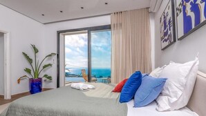 A hotel room with a bed, a potted plant, a view of the sea, and artwork on the wall.