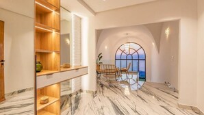 A modern interior with a marble floor, wooden shelving, a dining area with chairs, and a large arched window.