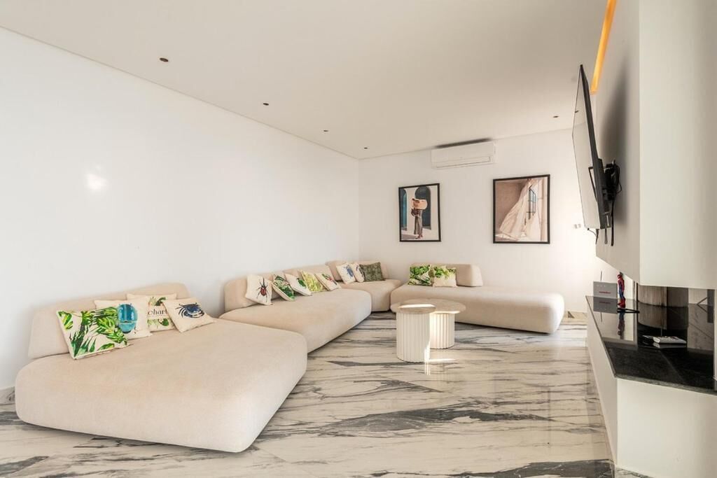 A modern living room with a sectional sofa, a small coffee table, and a flat-screen TV mounted on the wall.