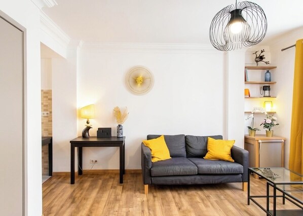 A living room with a sofa, a table, a lamp, a decorative wall piece, and a hanging light fixture.
