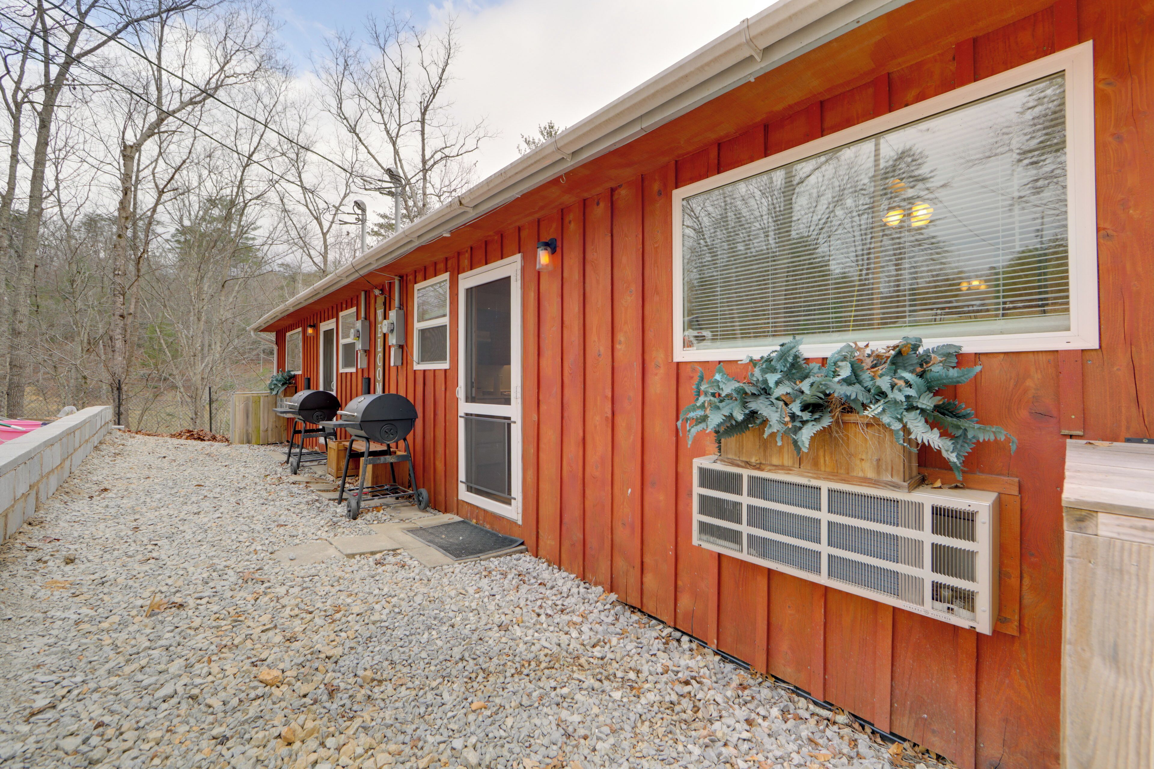 A wooden cabin with a gravel driveway, a grill, and a large window.