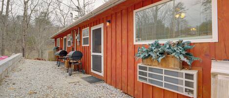 A wooden cabin with a gravel driveway, a grill, and a large window.