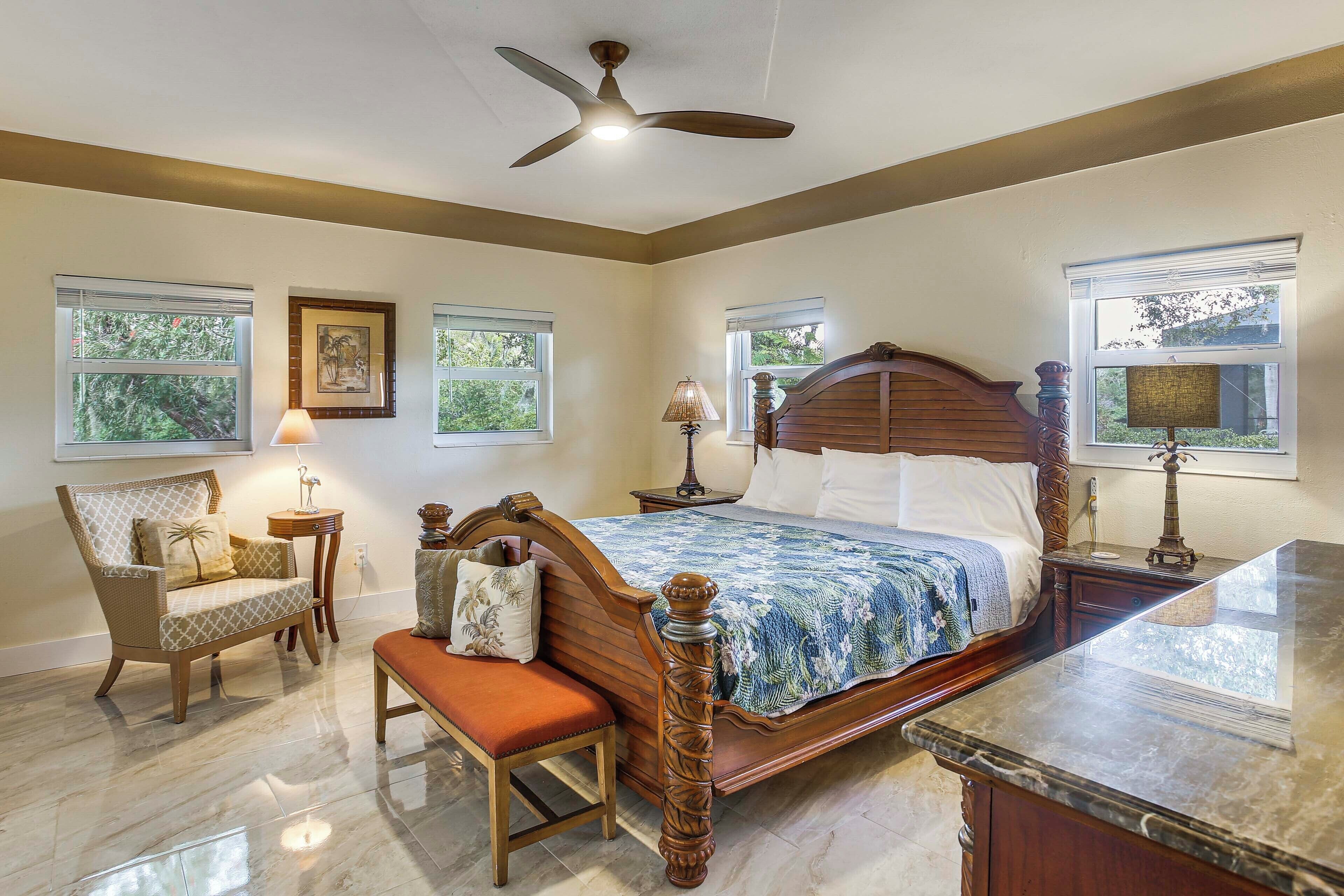 A bedroom with a bed, a chair, a bench, a nightstand, a lamp, and a ceiling fan.