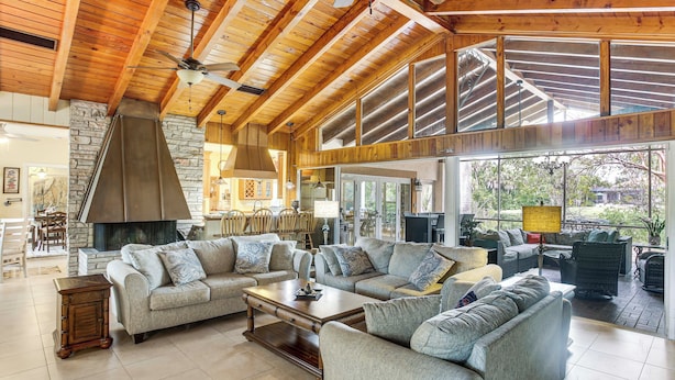 A spacious living room with a high ceiling, stone wall, and large windows. - Private Pool & Dock: Riverfront 'bridge Escape' (North Fort Myers)