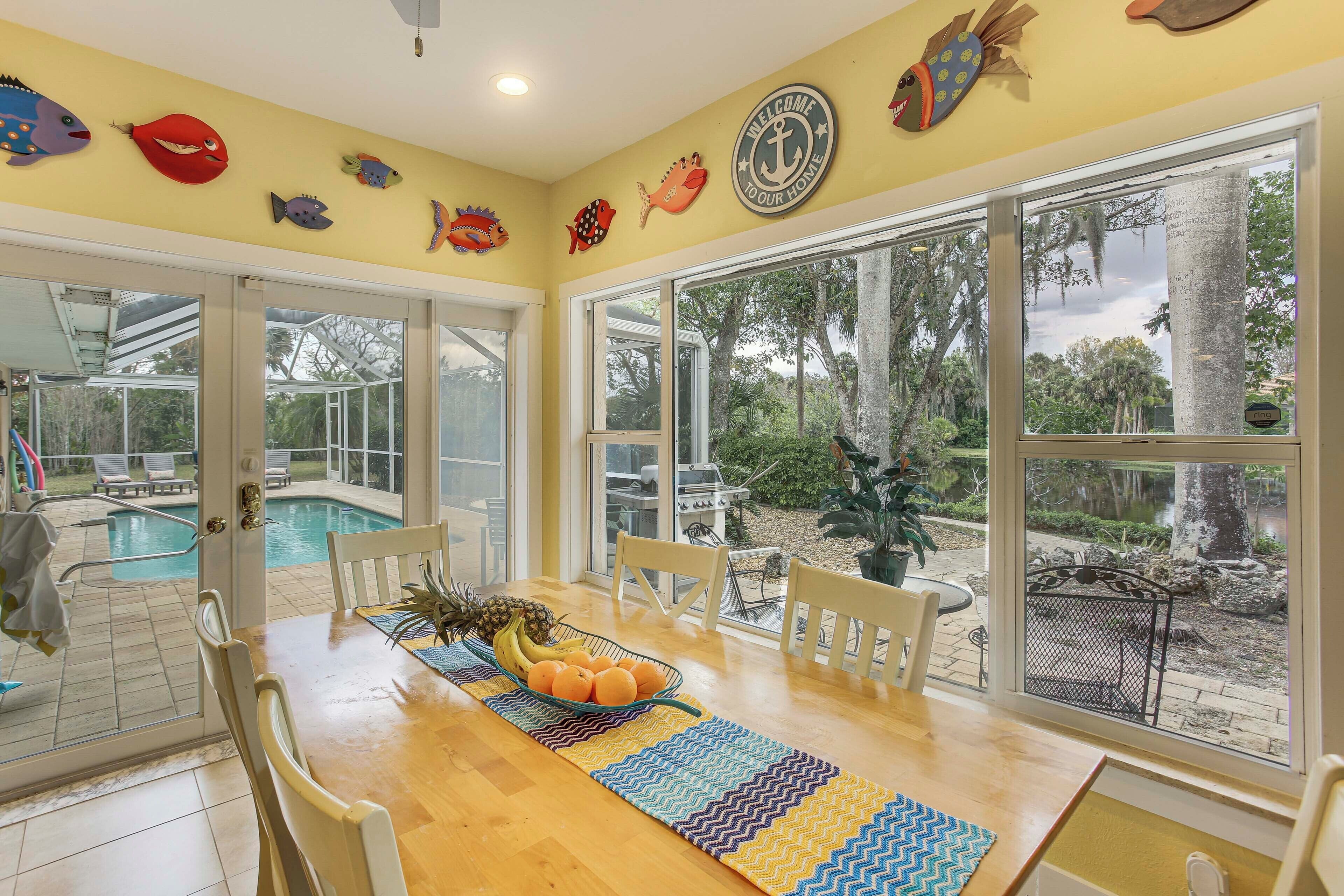 A dining area with a wooden table, chairs, a fruit bowl, and a view of the outdoor pool and garden.