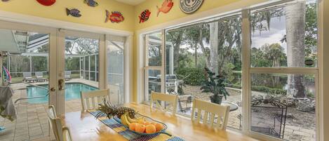 A dining area with a wooden table, chairs, a fruit bowl, and a view of the outdoor pool and garden.