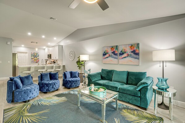 A modern living room with a teal sofa, blue armchairs, a glass coffee table, and a kitchen in the background. - Canal-front Gem! 7 Mi to Port Charlotte Beach Park (Port Charlotte)