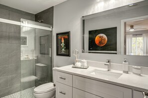 A modern bathroom with a glass shower enclosure, a toilet, a sink with a mirror, and artwork on the wall. - Canal-front Gem! 7 Mi to Port Charlotte Beach Park (Port Charlotte)