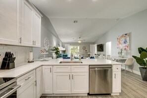 A modern kitchen with white cabinetry, a stainless steel dishwasher, and a large island with a sink. - Canal-front Gem! 7 Mi to Port Charlotte Beach Park (Port Charlotte)
