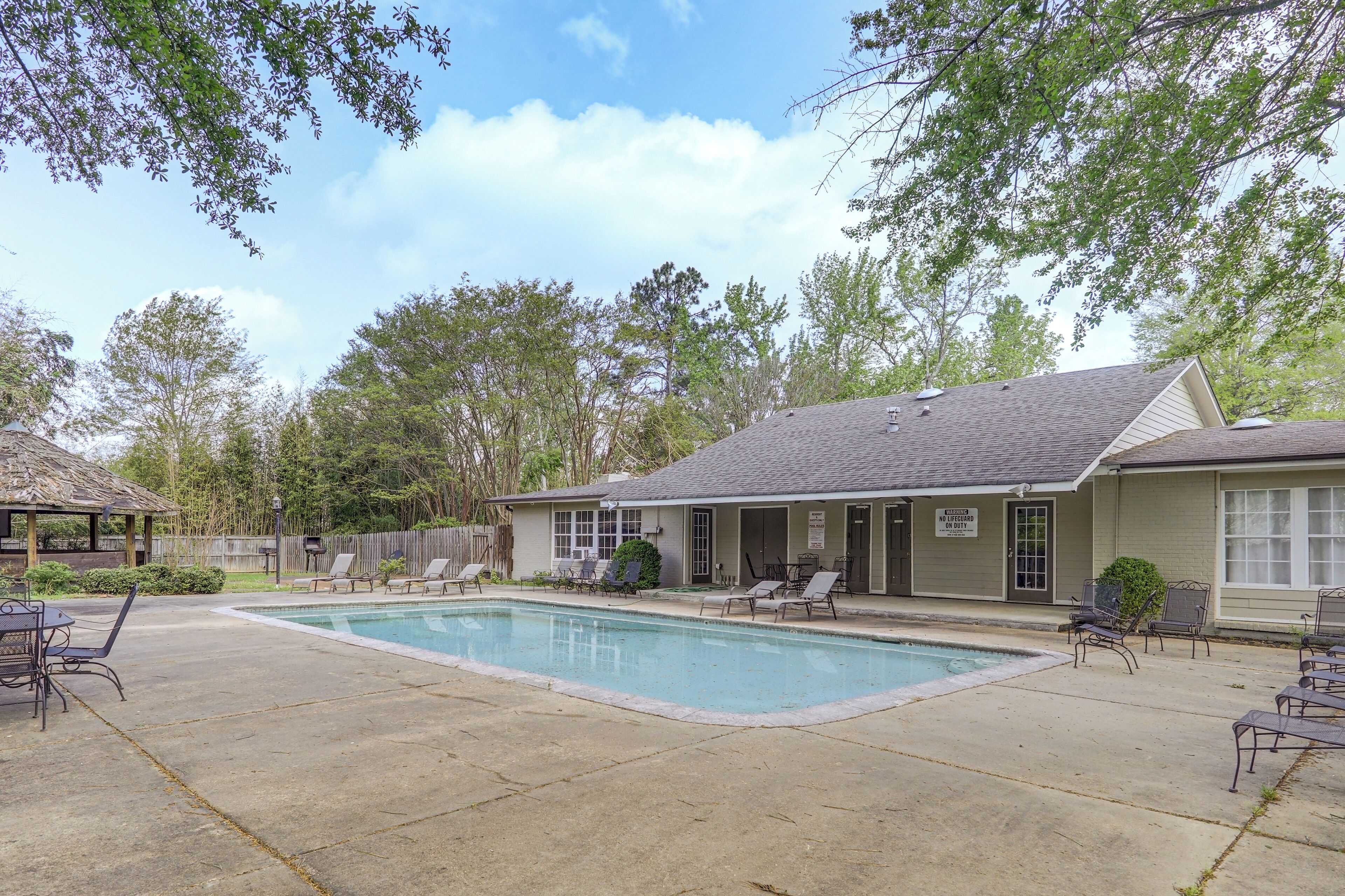 A pool area with lounge chairs, a covered seating area, and a building with a sign.