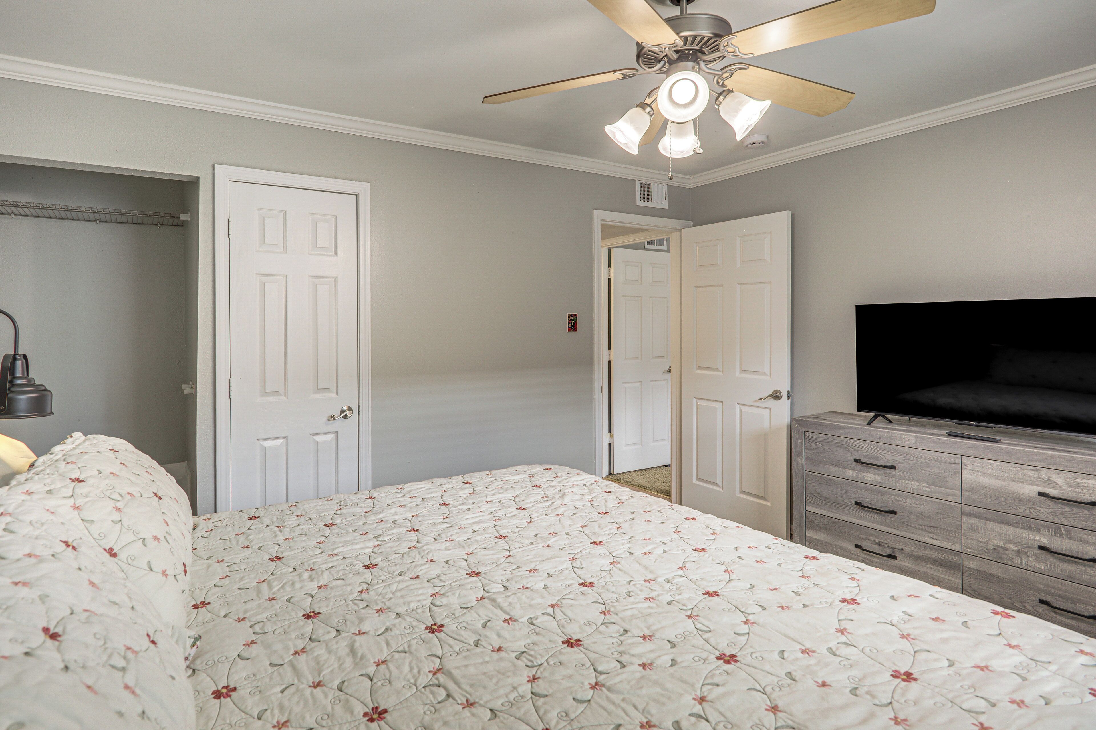 Une chambre à coucher comprenant un lit, une commode, un ventilateur de plafond et un téléviseur.