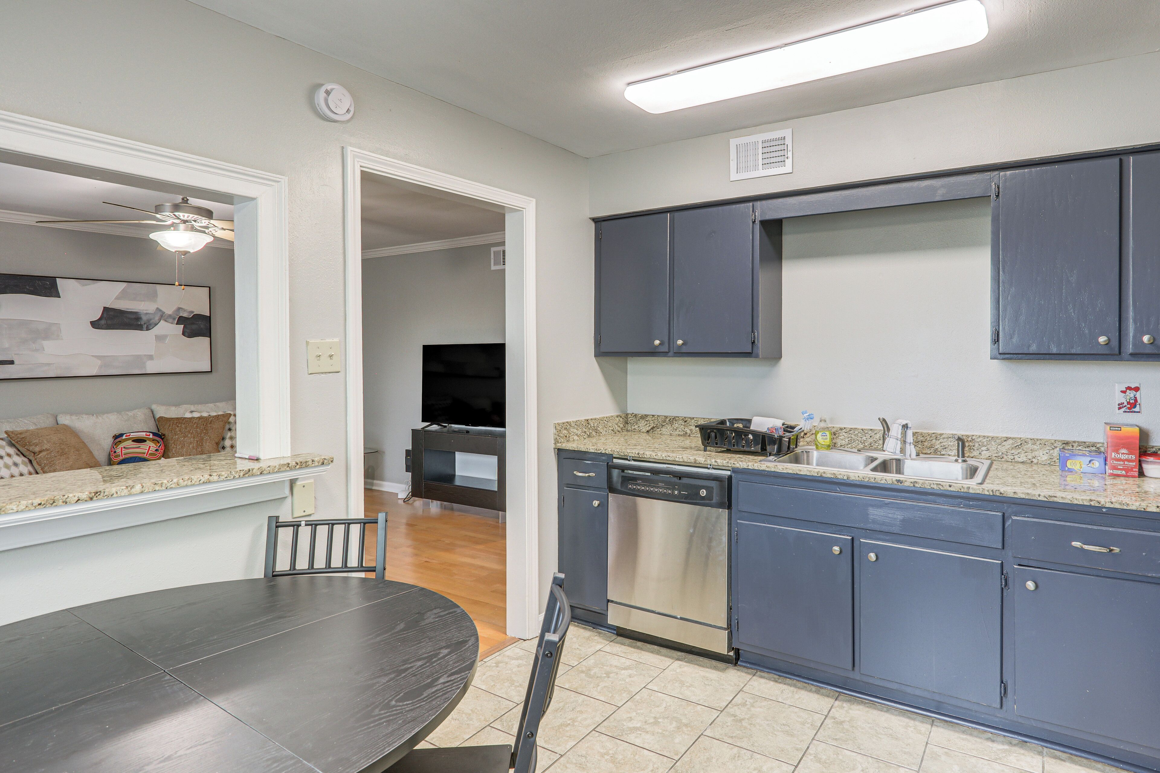 A kitchen with dark cabinets, a dishwasher, and a dining area with a table and chairs.