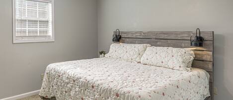 Un dormitorio con cabecera de madera, colcha estampada, ventilador de techo y ventana con persianas.