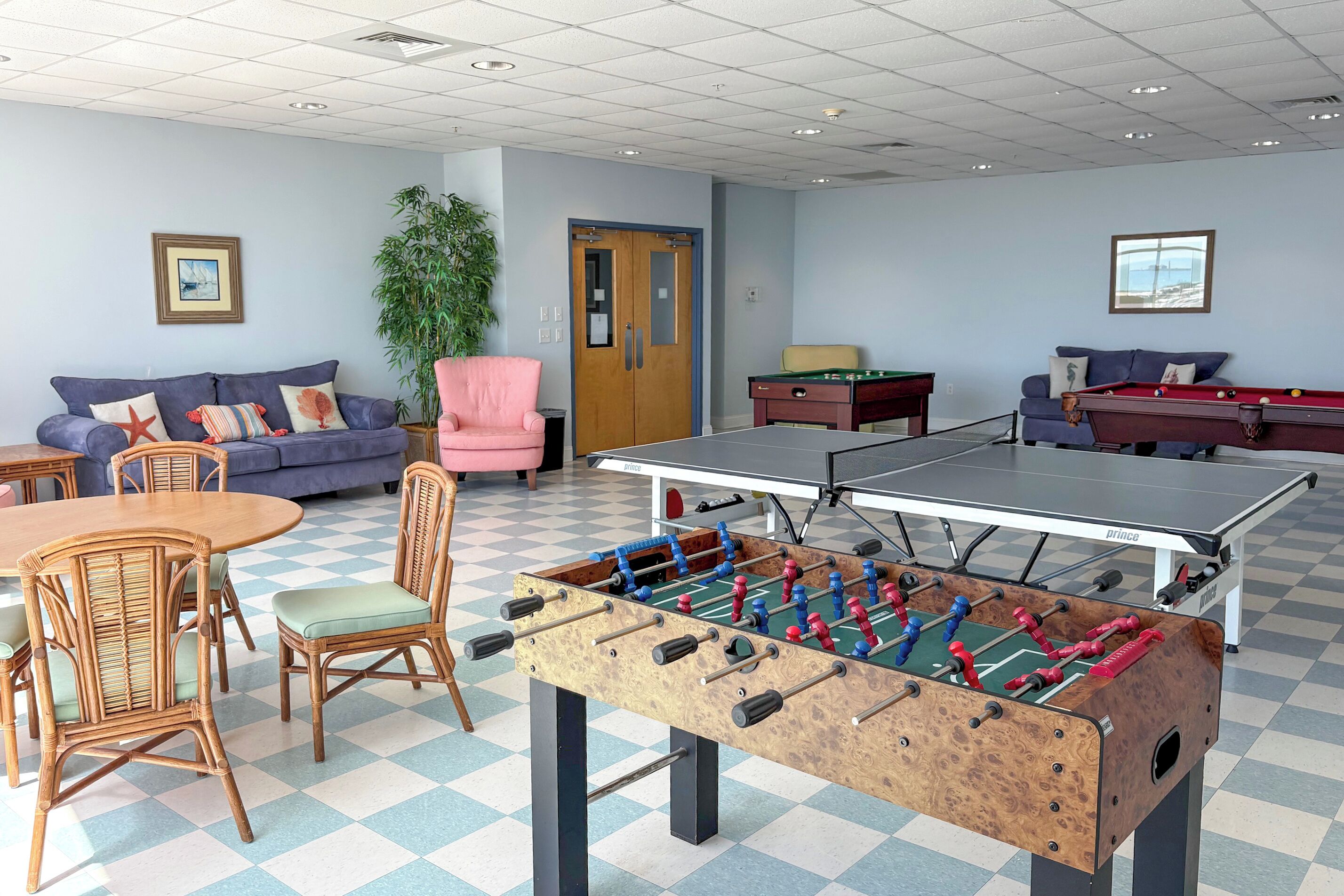 A room with a foosball table, two sofas, a pool table, and a dining table with chairs.