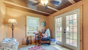 Une pièce confortable avec un ventilateur de plafond, un lit, une chaise, une fenêtre avec des stores et une vue sur une terrasse.