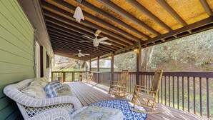 Une terrasse extérieure couverte, aménagée avec des meubles en osier, des ventilateurs de plafond et offrant une vue sur les arbres environnants.