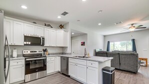 A modern kitchen with white cabinetry, stainless steel appliances, and a grey sofa in the adjacent living area. - Dunnellon Escape w/ Yard: 8 Mi to Rainbow River (Dunnellon)
