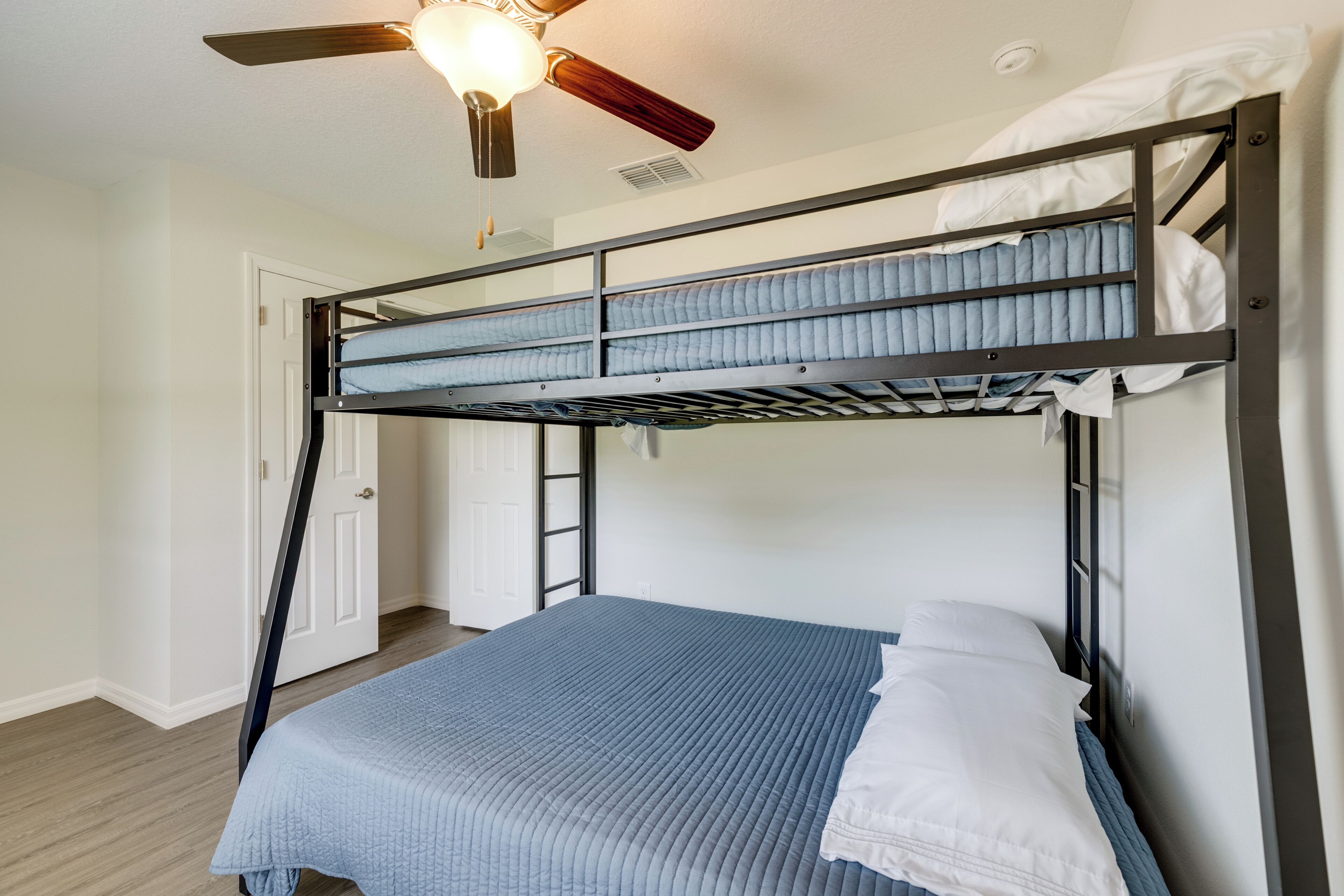 A bunk bed room with a ceiling fan, a door, and a window.
