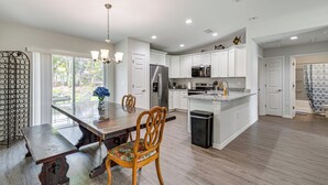 A modern kitchen with white cabinets, a stainless steel refrigerator, and a dining area with a wooden table and chairs. - Dunnellon Escape w/ Yard: 8 Mi to Rainbow River (Dunnellon)