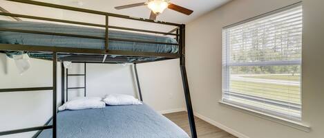 A bunk bed with a ceiling fan, a window with blinds, and a wooden floor.