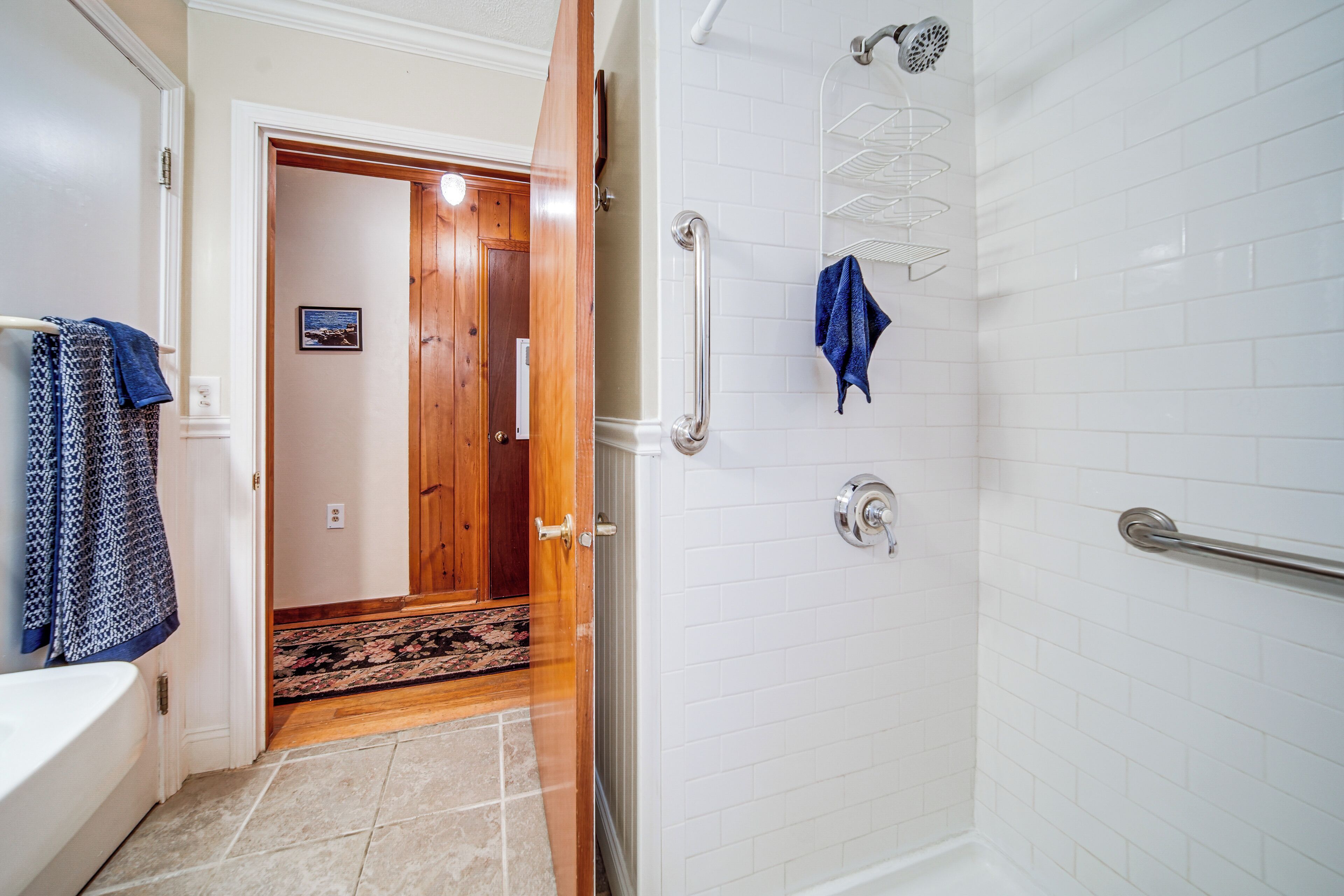 Un baño con ducha, un perchero y una puerta que da a otra habitación.