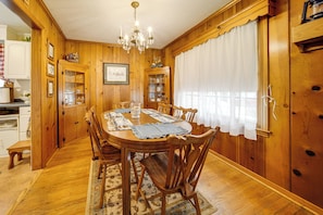 A wooden dining room with a chandelier, a table set for six, and a patterned rug. - Walk to Edinboro Lake: Cozy Cottage w/ Porch! (Edinboro)