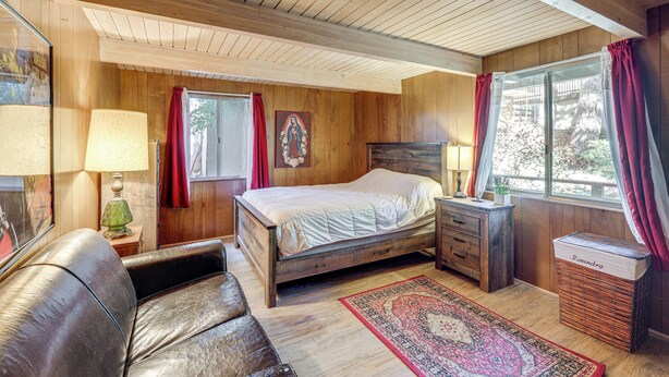 Une chambre à coucher aux murs lambrés, avec un lit, une table de chevet, une lampe et une fenêtre avec des rideaux.