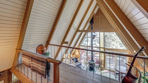 Une pièce aux hauts plafonds, avec des poutres en bois, un escalier et une vue sur l’extérieur.