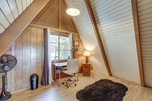 A room with a sloped ceiling, a desk with a chair, a standing fan, a trash bin, and a lamp. - Running Springs Retreat: Ski, Hike & Relax! (Running Springs)