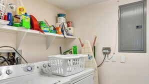 A laundry area with a washing machine, shelves with cleaning supplies, and a utility meter. - Resort-style Fort Myers Gem: Swim, Golf & Cruise! (Fort Myers)