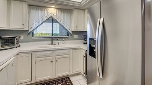 A kitchen with white cabinets, a stainless steel refrigerator, a built-in oven, and a window with a valance. - Resort-style Fort Myers Gem: Swim, Golf & Cruise! (Fort Myers)