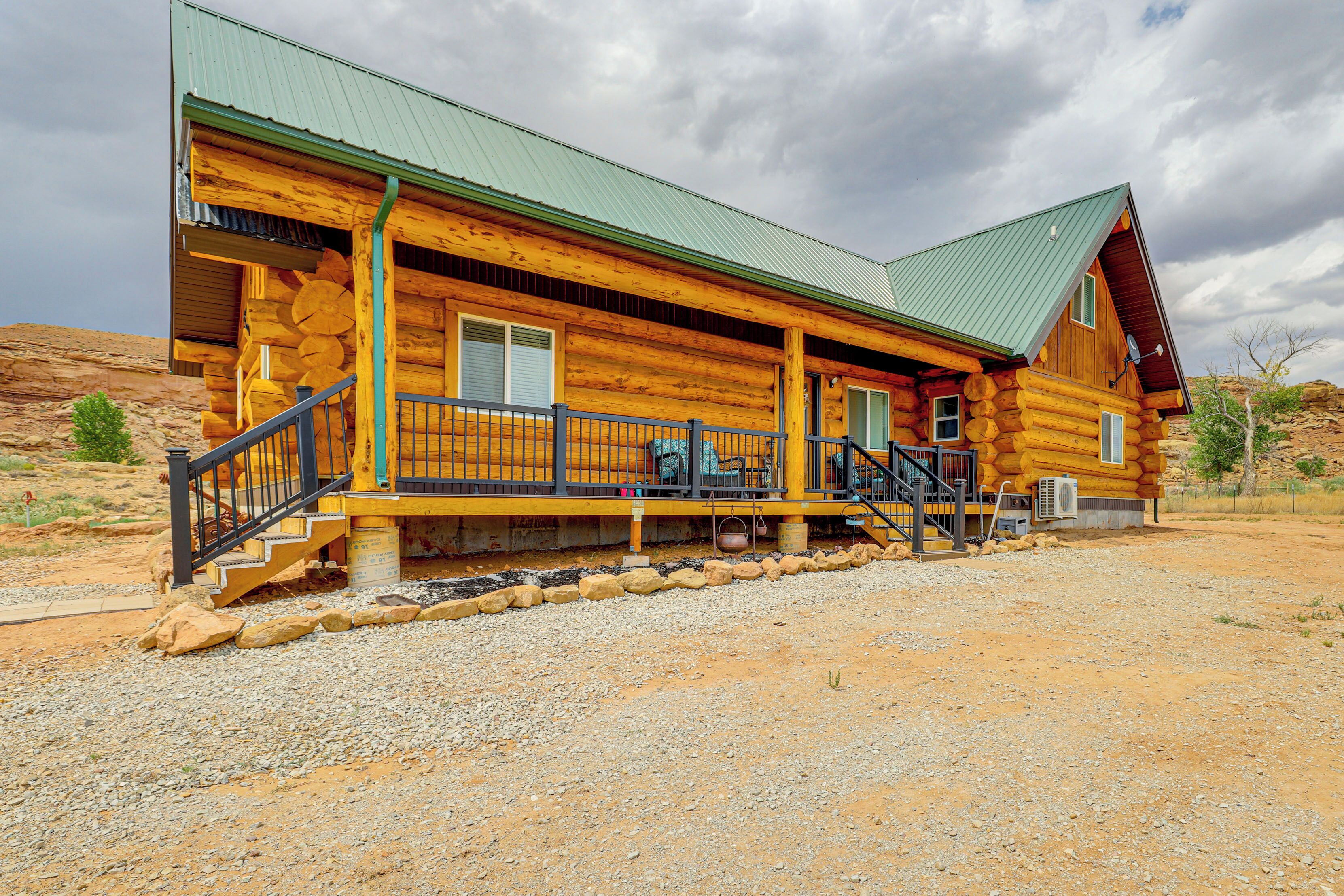 A log cabin with a porch, a staircase, and a green roof.