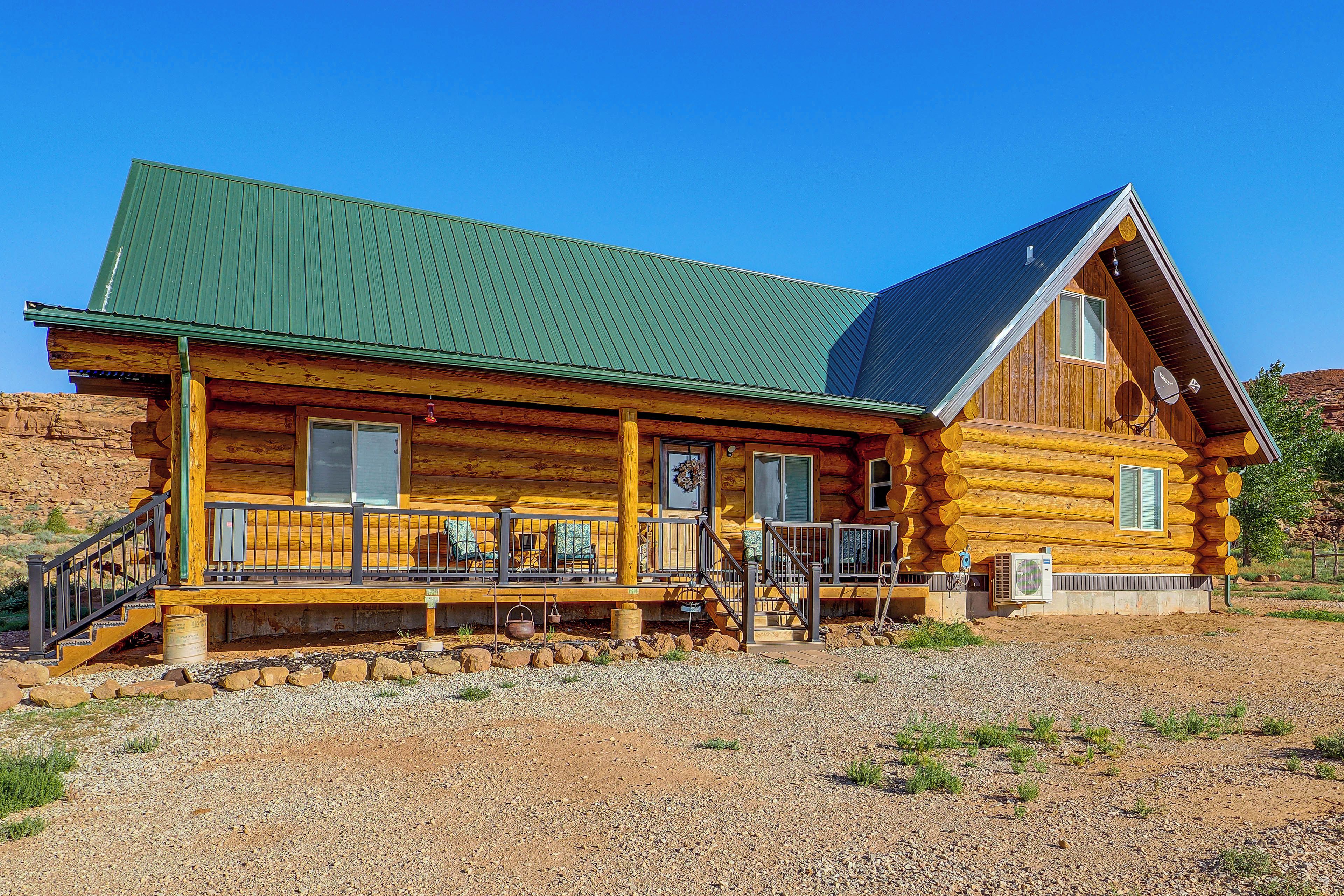 Une cabane en rondins avec un toit végétalisé, une véranda dotée de sièges d’extérieur et une grande fenêtre.