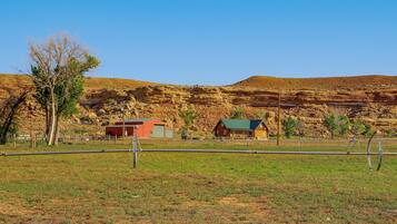 A rural landscape with a red barn, a wooden cabin, and a clear blue sky.