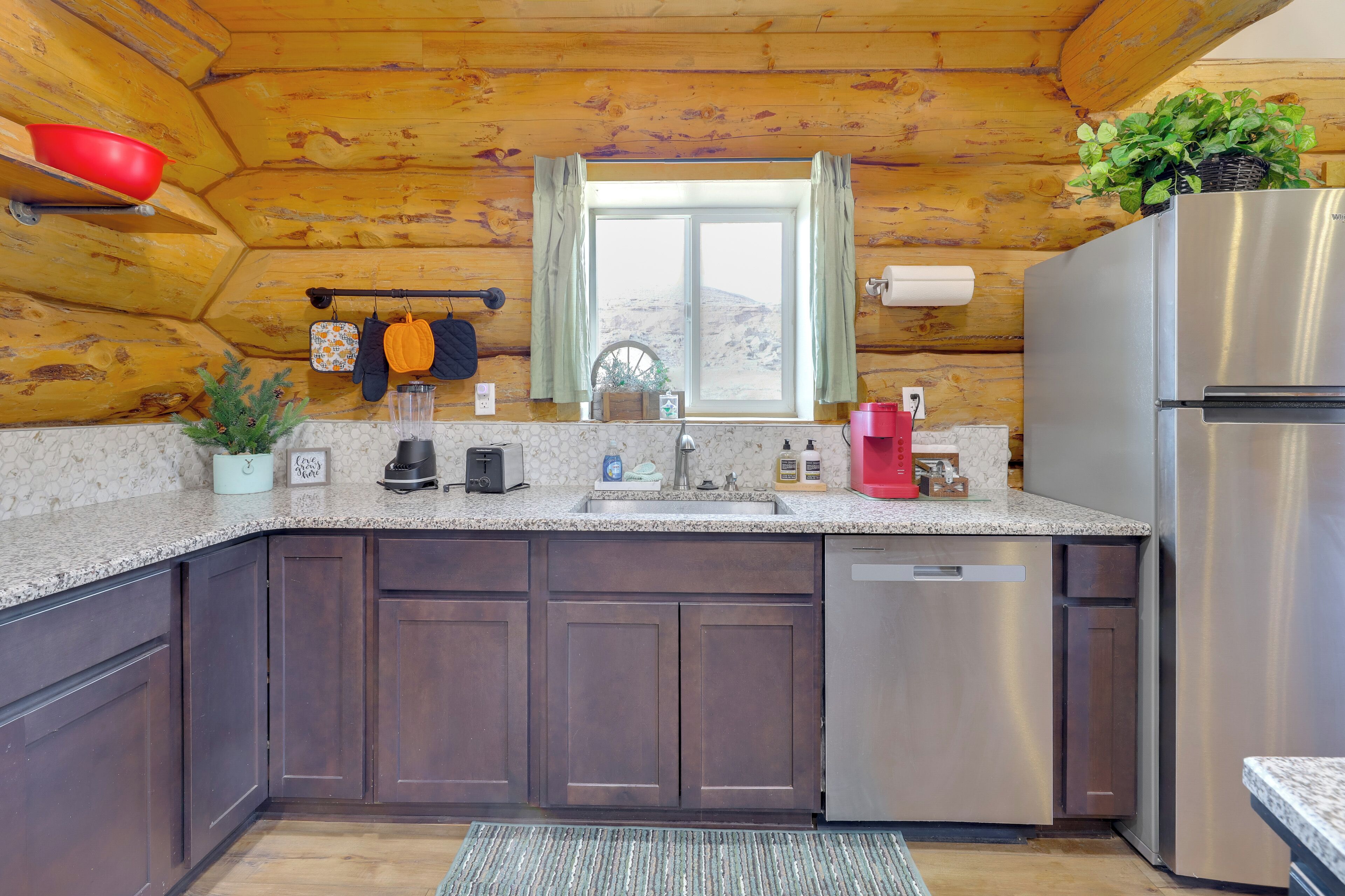 A kitchen with wooden walls, a stainless steel refrigerator, a sink, and a window with curtains.