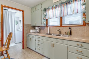 A kitchen with light green cabinets, a wooden chair, a sink, and a window with striped curtains. - 7 Mi to Mississinewa Lake! Charming Home (Converse)