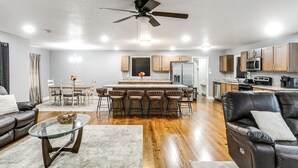 A modern living room with a glass coffee table, leather sofa, and a dining area with a bar stool setup.