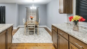 A kitchen with wooden cabinets, a marble countertop, a dining table with chairs, and a vase with flowers.