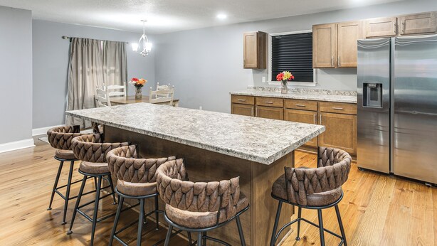 A kitchen with a central island, bar stools, wooden cabinets, and stainless steel appliances.
