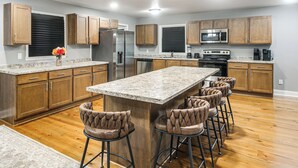 A modern kitchen with wooden cabinets, a central island with bar stools, stainless steel appliances, and a granite countertop.