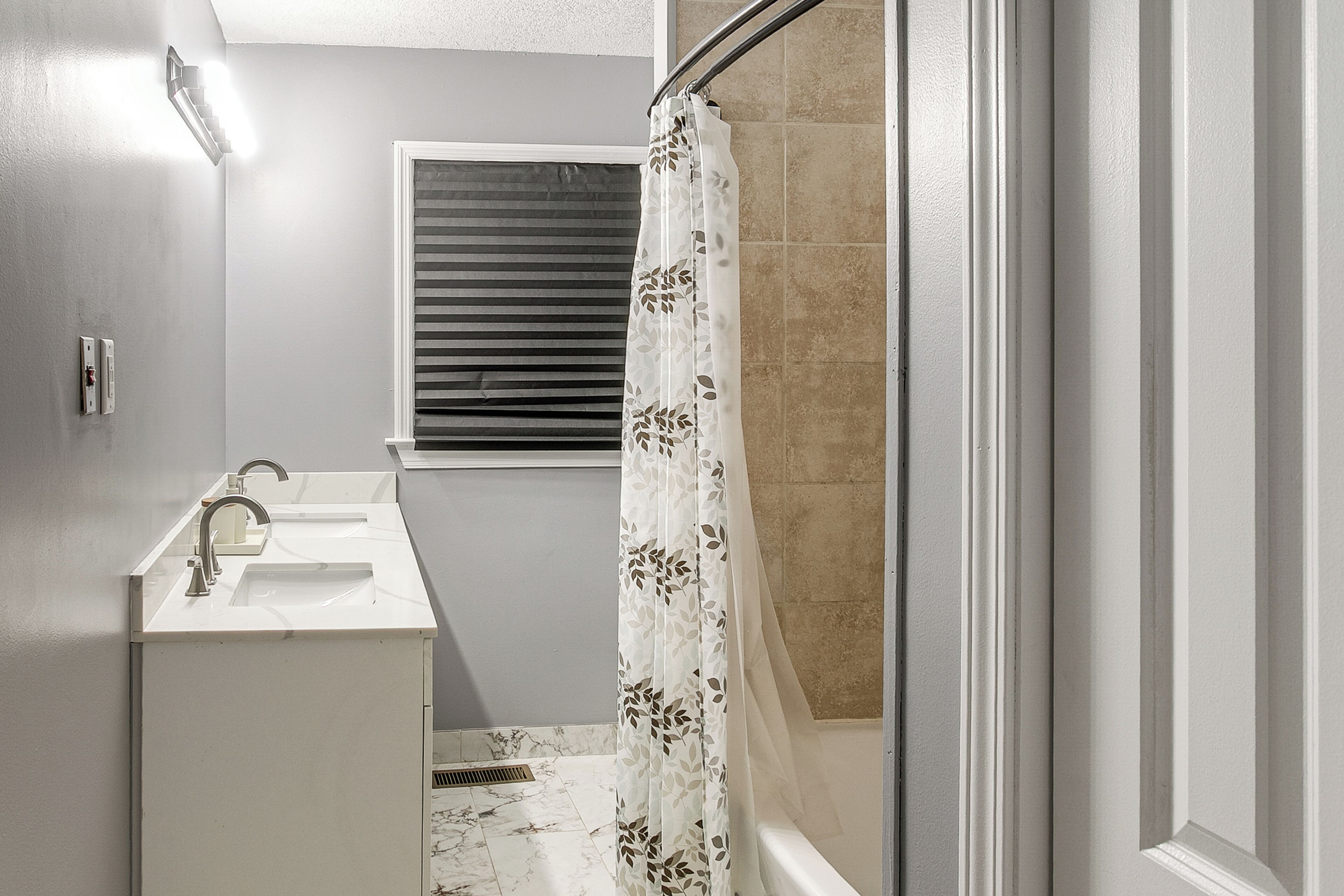 A bathroom with a sink, a shower curtain, and a window with blinds.