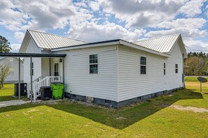 Uma casa térrea branca com varanda, antena parabólica e uma lixeira verde.