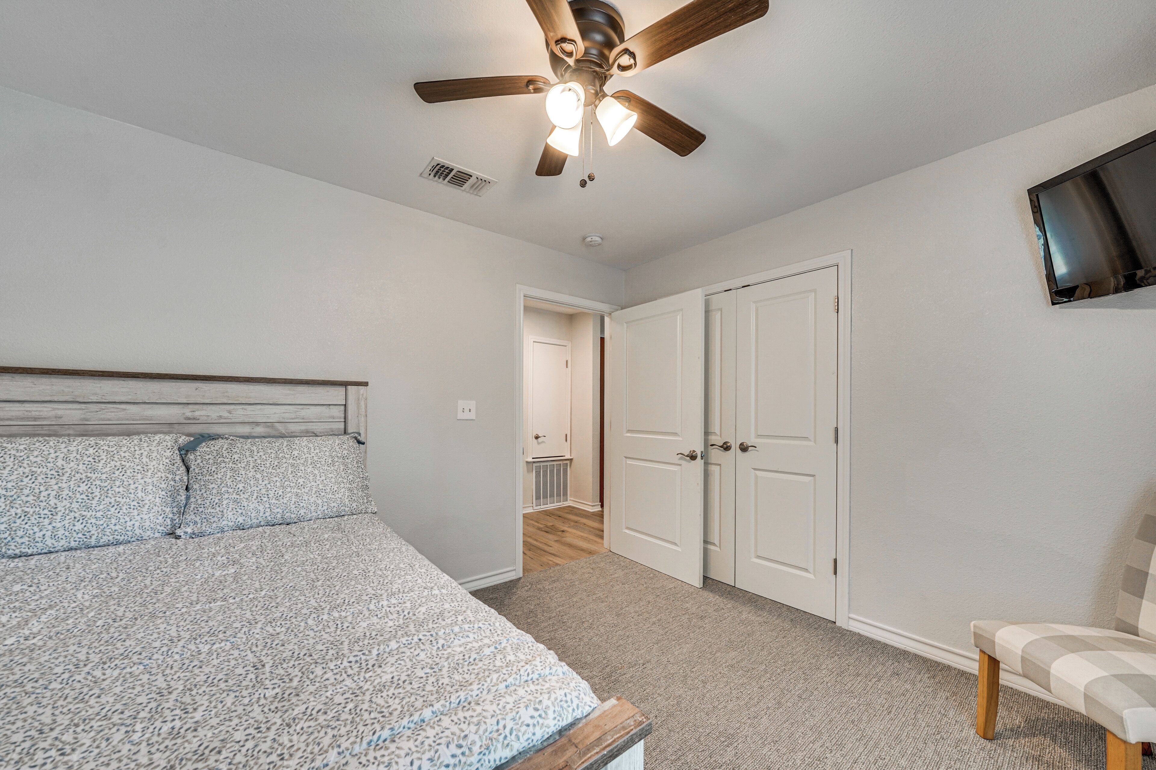Un dormitorio con cama, ventilador de techo, televisor y puerta que da a otra habitación.