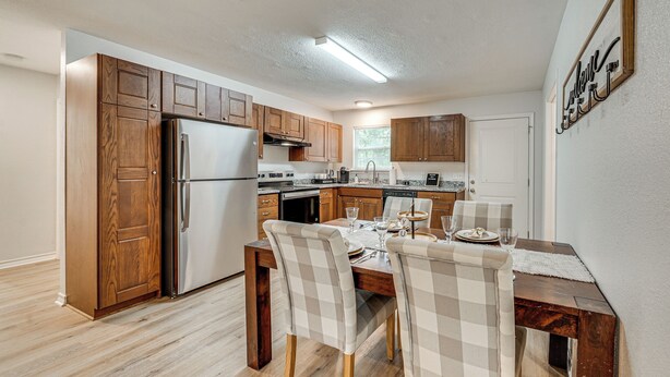 Una cocina moderna con armarios de madera, un refrigerador de acero inoxidable y un comedor con sillas a cuadros y una mesa dispuesta para dos.