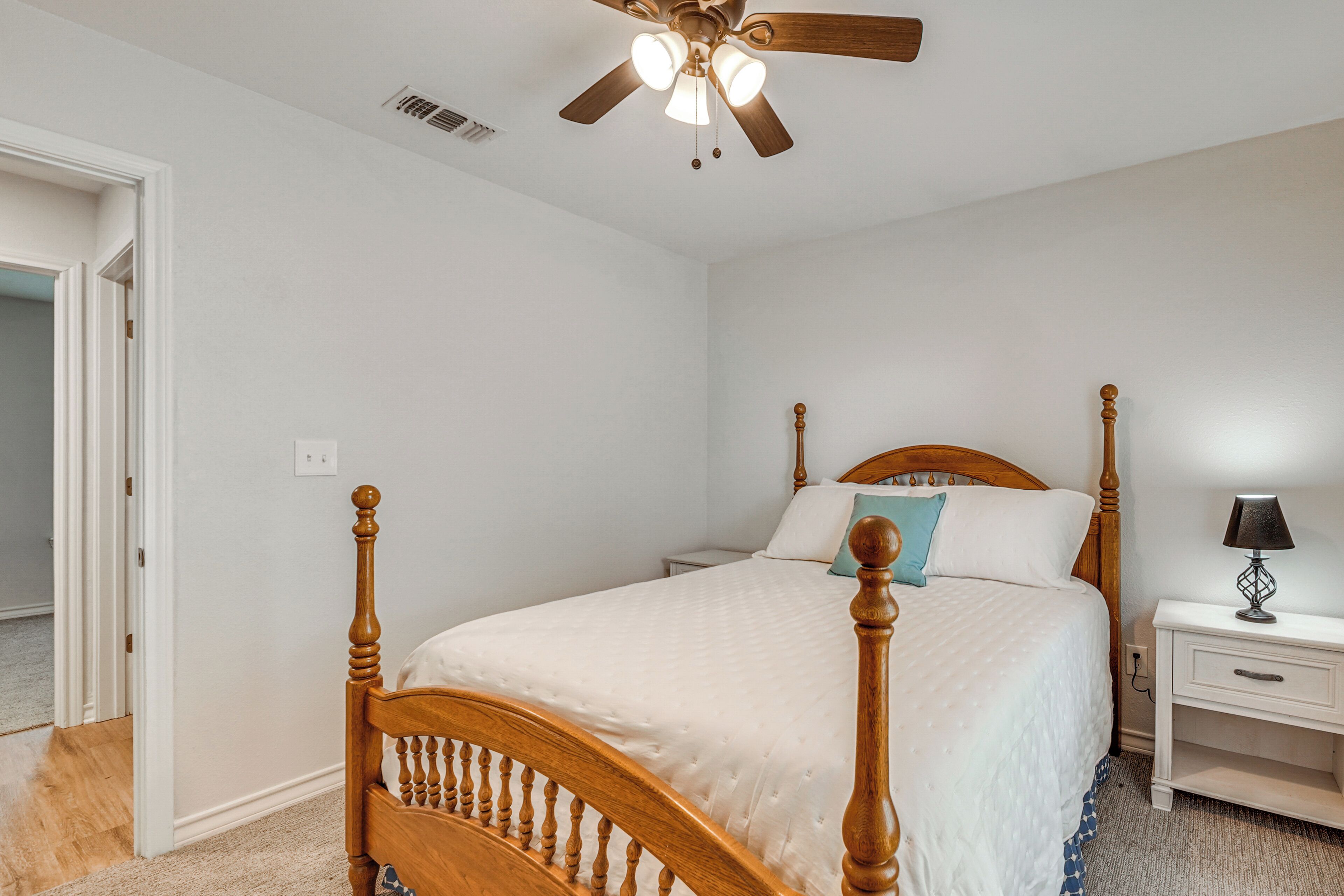A bedroom with a wooden bed, a nightstand, a ceiling fan, and a door leading to another room.