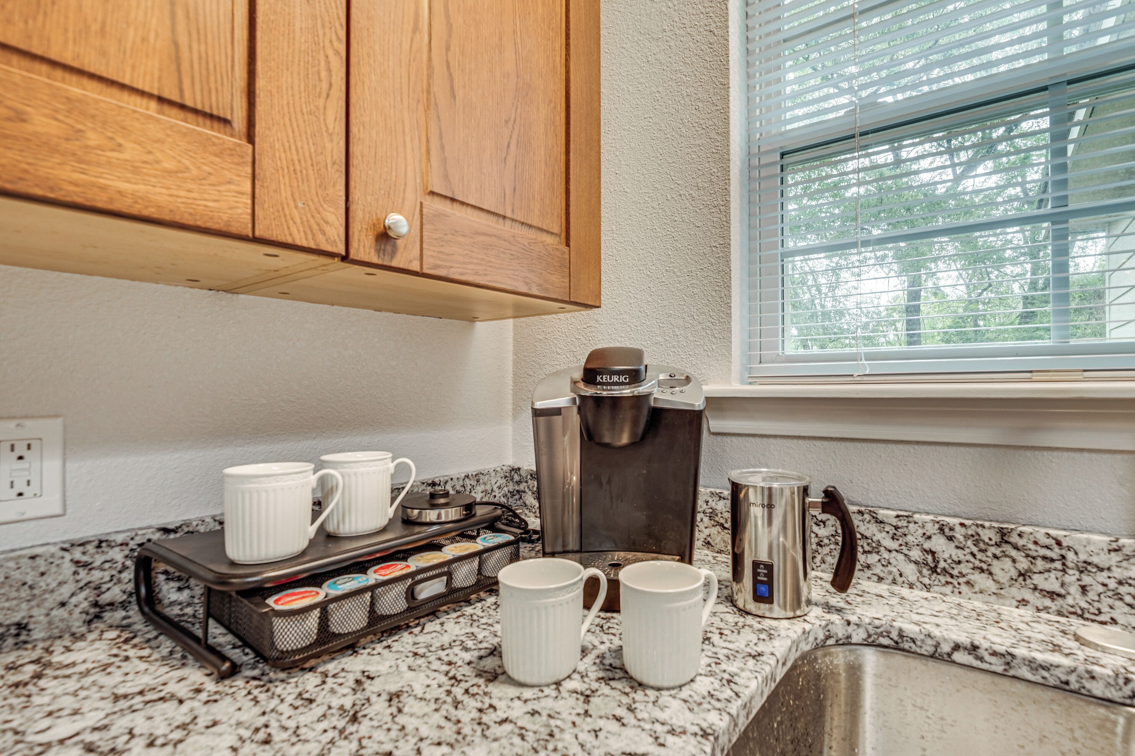 A kitchen with a coffee maker, mugs, and a coffee pot on the counter.