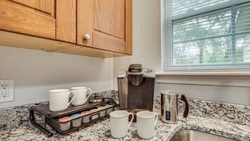 A kitchen with a coffee maker, mugs, and a coffee pot on the counter.