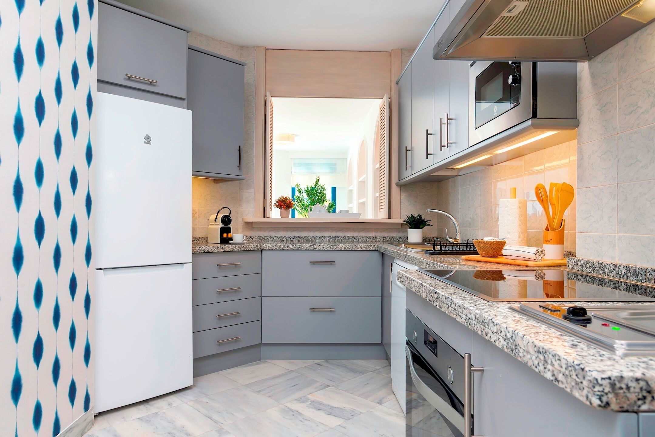 Een moderne keuken met grijze kastjes, een inbouwoven en een raam met uitzicht op een straat.